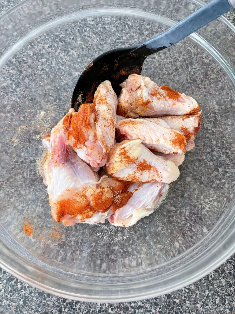 Chicken wings coated in spices in a glass bowl.