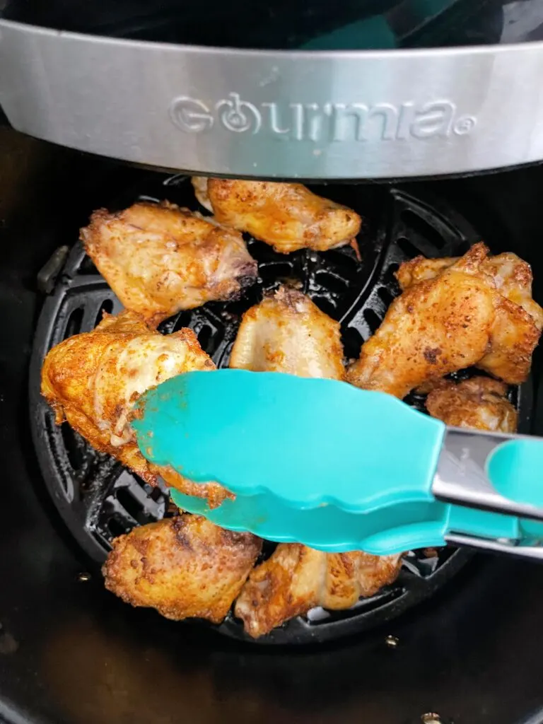 Tongs flipping over a chicken wing in an air fryer.