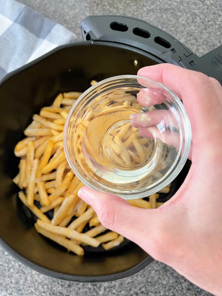 Oil and an air fryer basket filled with frozen fries.