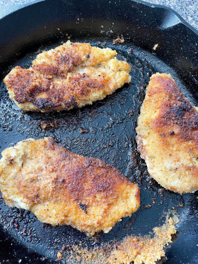 Chicken with golden brown beading in a cast iron skillet.