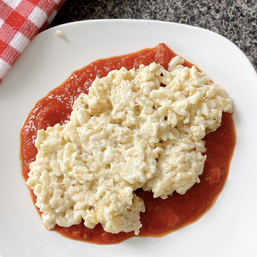 Creamy parmesan risotto with tomato basil sauce on a white plate.