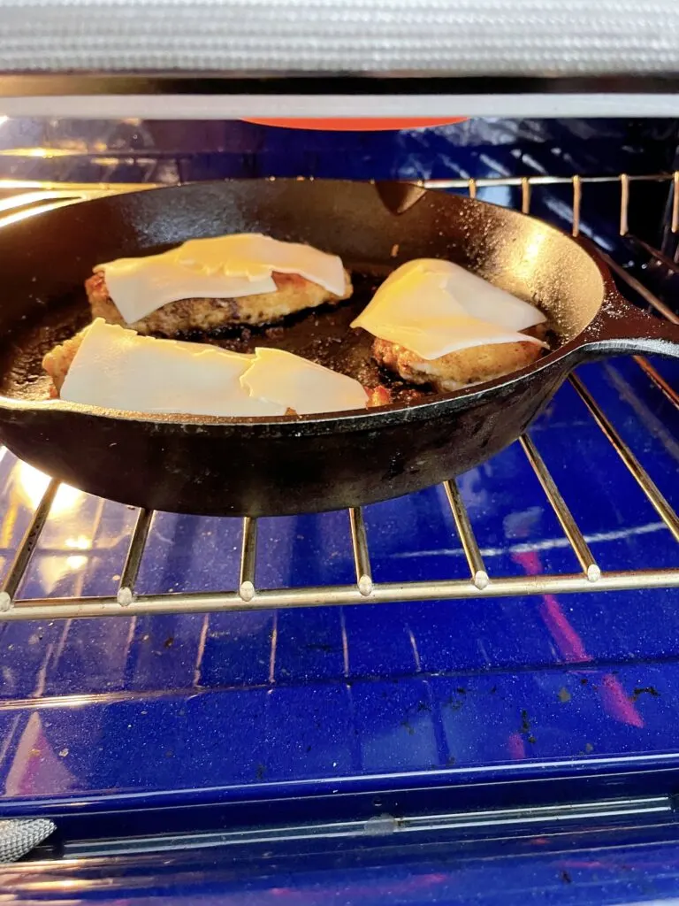 Chicken parmesan in a skillet under a broiler.