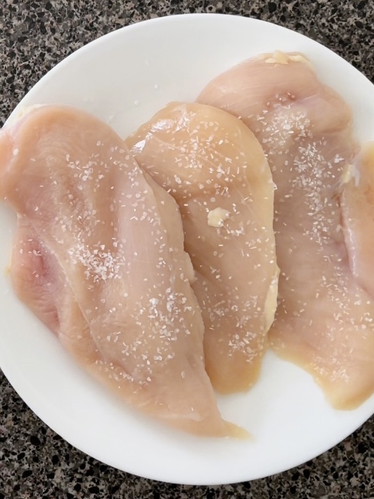 Raw chicken breasts on a white plate.