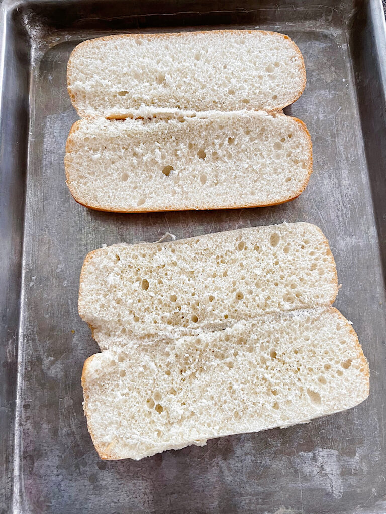 Sandwich rolls sliced open on a baking sheet/