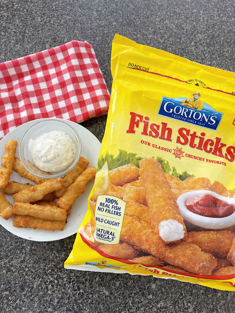 A bag of frozen fish sticks next to a plate of fish sticks cooked in an air fryer.