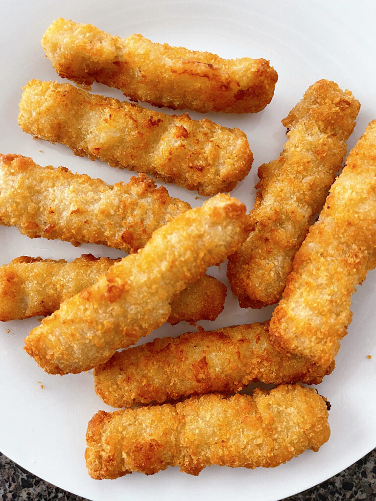 Fish sticks cooked in an air fryer on a white plate.