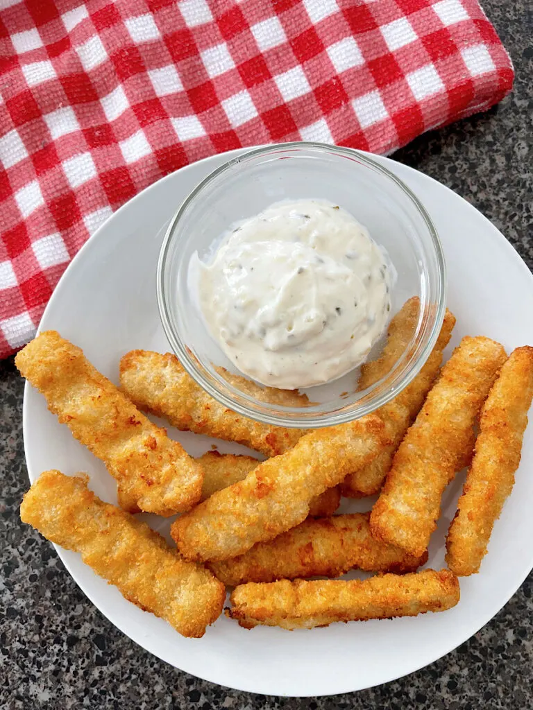 Fish sticks on a plate with a dish of tartar sauce.