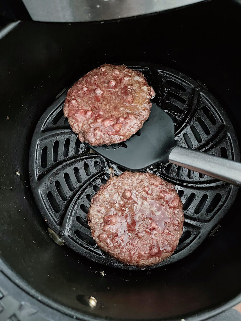 A spatula flipping an frozen burger in the air fryer.