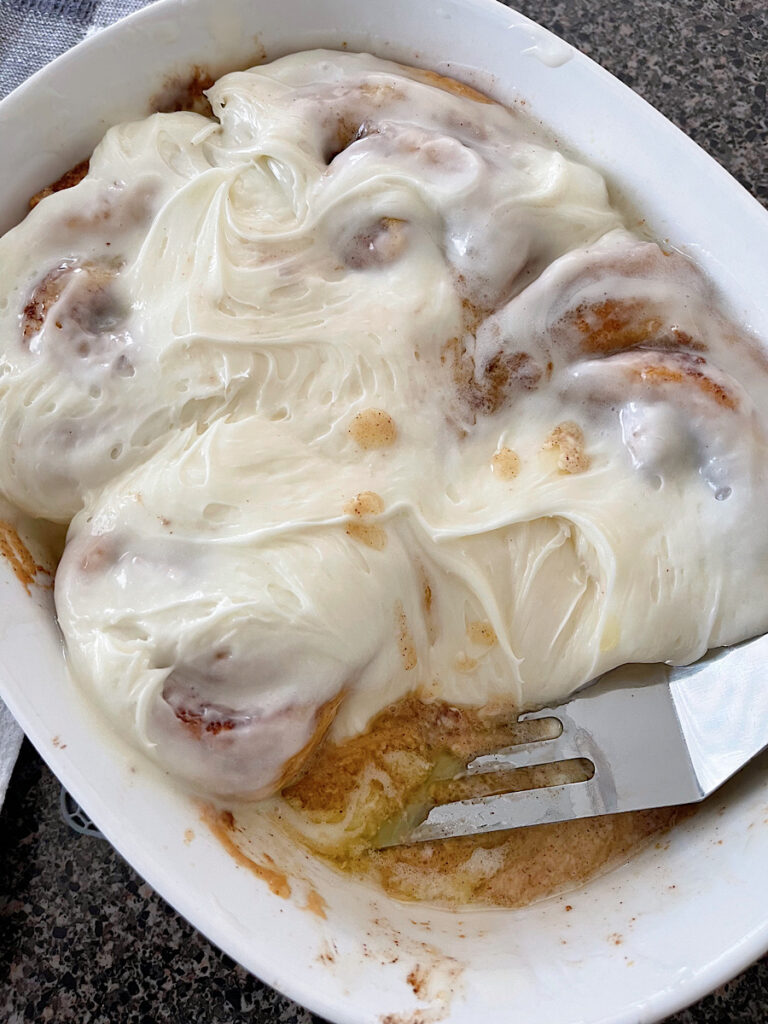 A baking dish full of cinnamon rolls with heavy cream and cream cheese frosting.