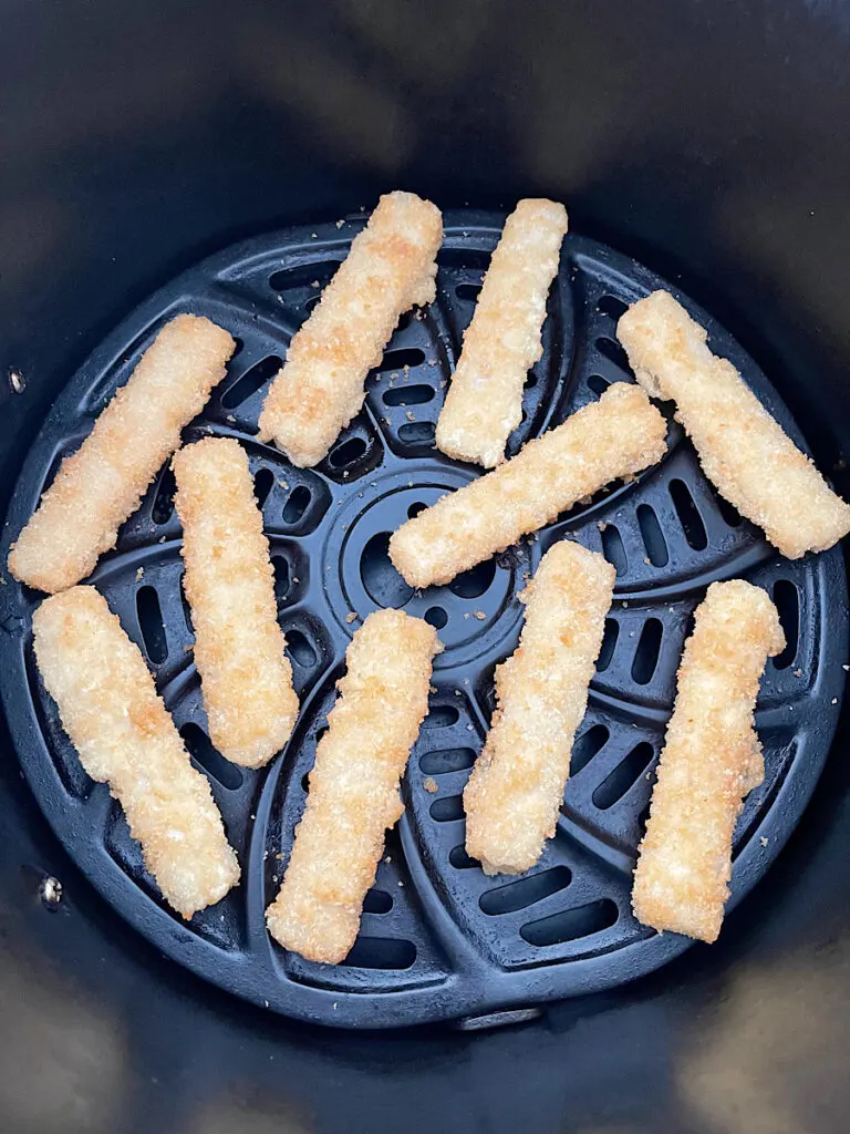 Frozen fish sticks in an air fryer basket.