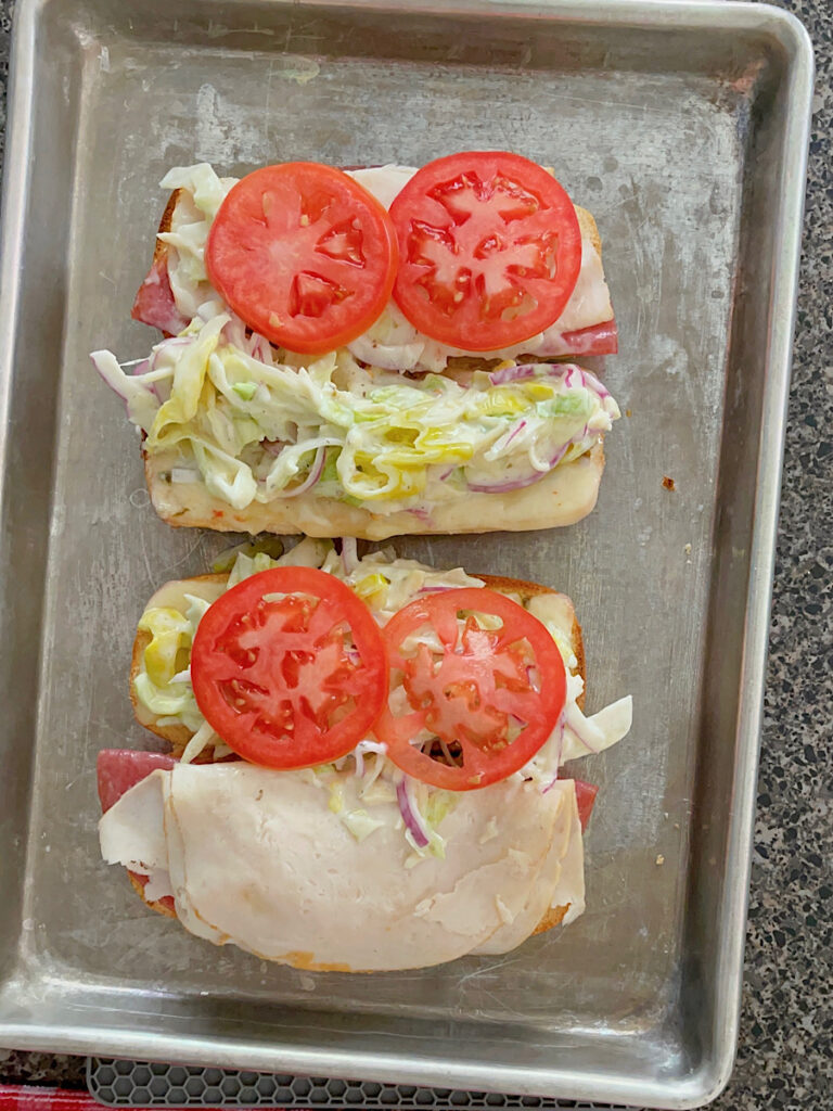 Toasted grinder sandwiches topped with grinder salad and tomato slices.