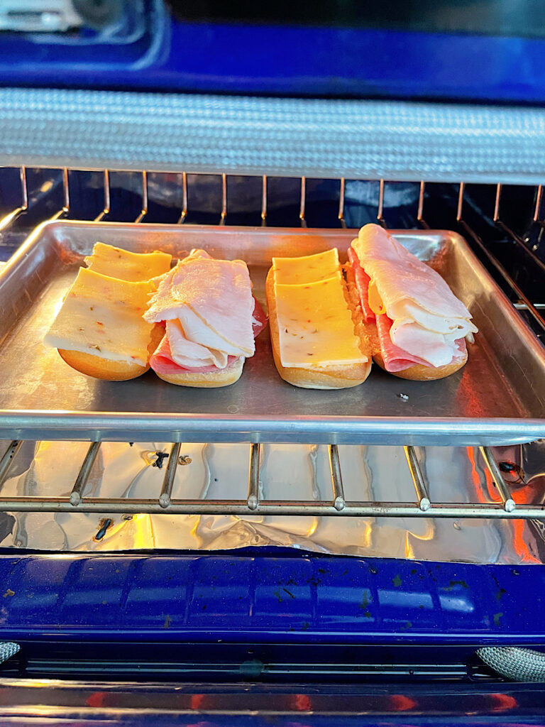 Two grinder sandwiches being toasted under a broiler.