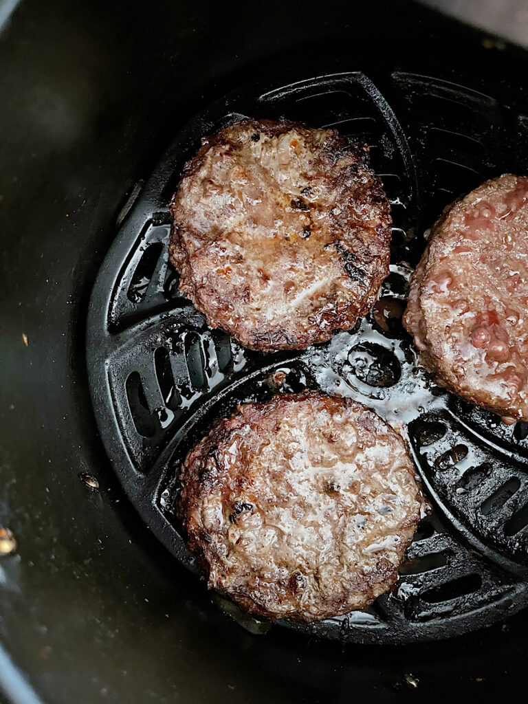 Three frozen hamburger patties in an air fryer basket.