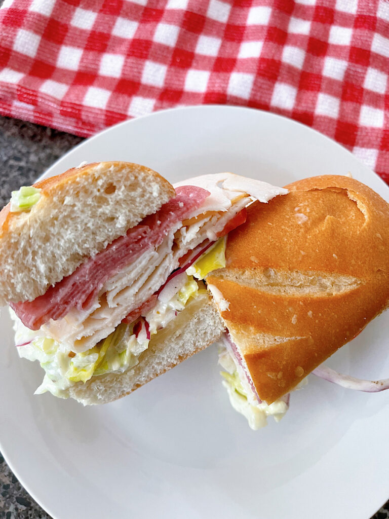 A TikTok grinder sandwich with meat, cheese, and grinder salad on a white plate with a red and white kitchen towel.