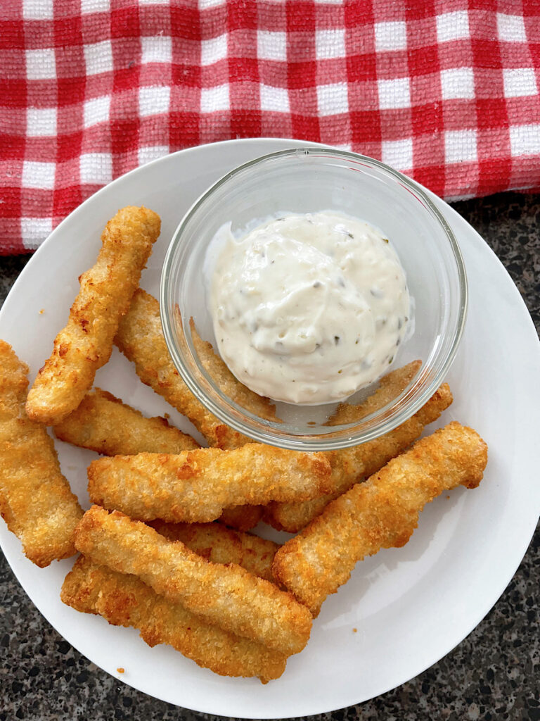 Fish sticks and a dish of tartar sauce on a white plate.