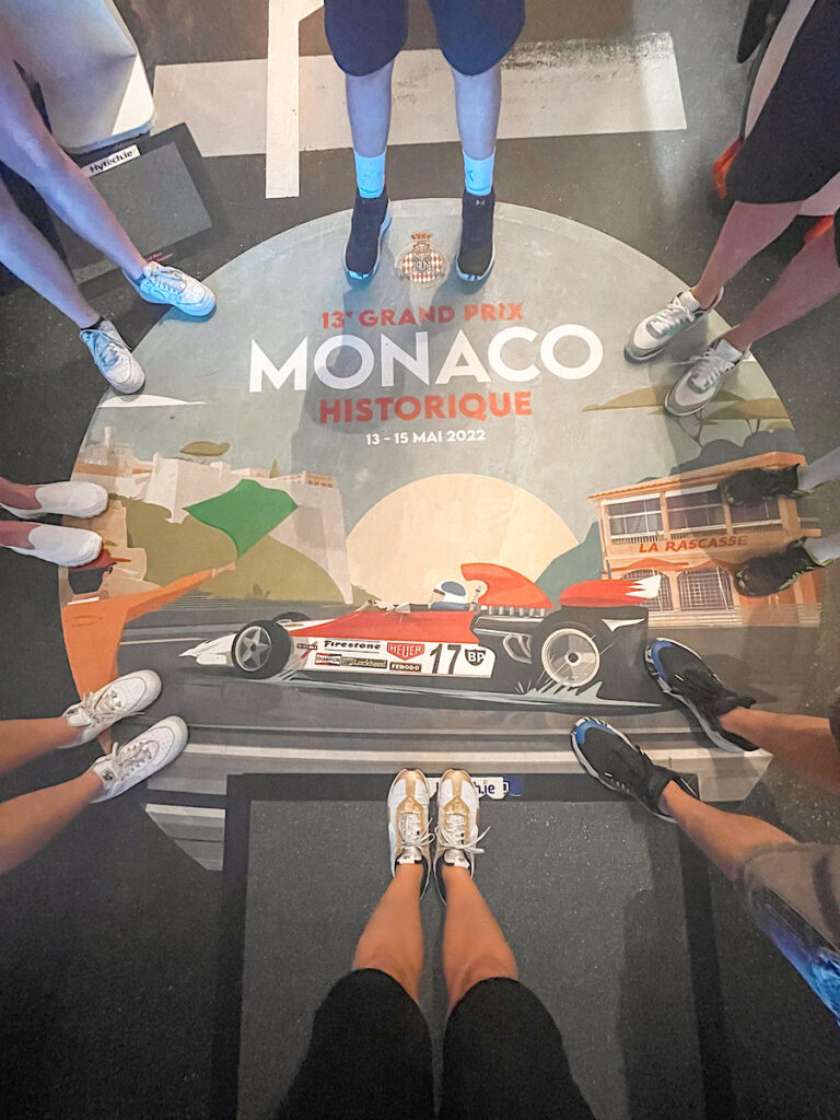 Feet standing around a sign with Monaco and an F1 car.