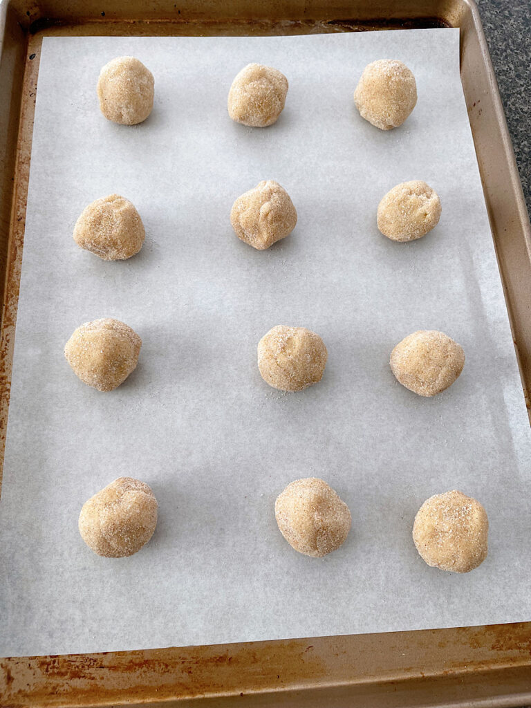 Balls of snickerdoodle cookie dough on a parchment paper lined baking sheet.