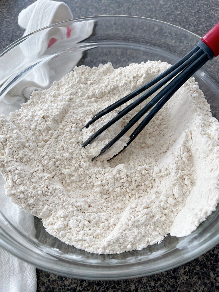 Snickerdoodle dry ingredients in a glass bowls with a black whisk.