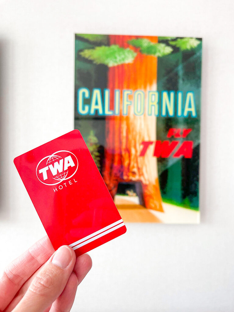 A TWA Hotel room key in front of a poster of California.