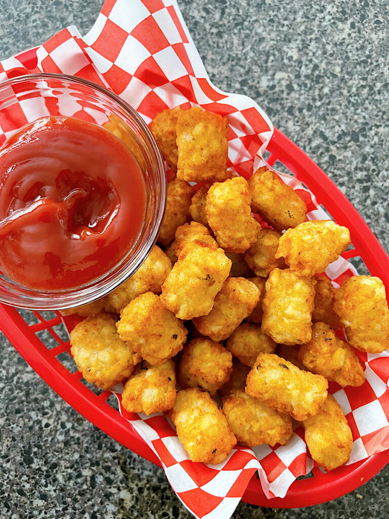 Air Fryer tater tots in a red basket with ketchup.