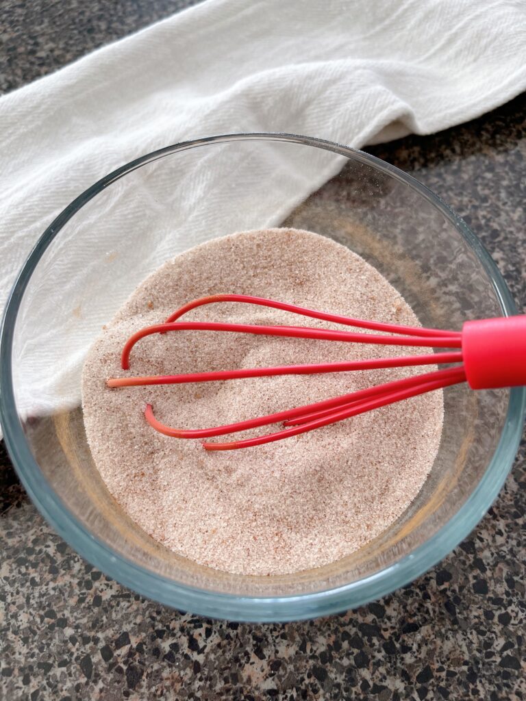 Cinnamon and sugar mixed together in a bowl with a red whisk.