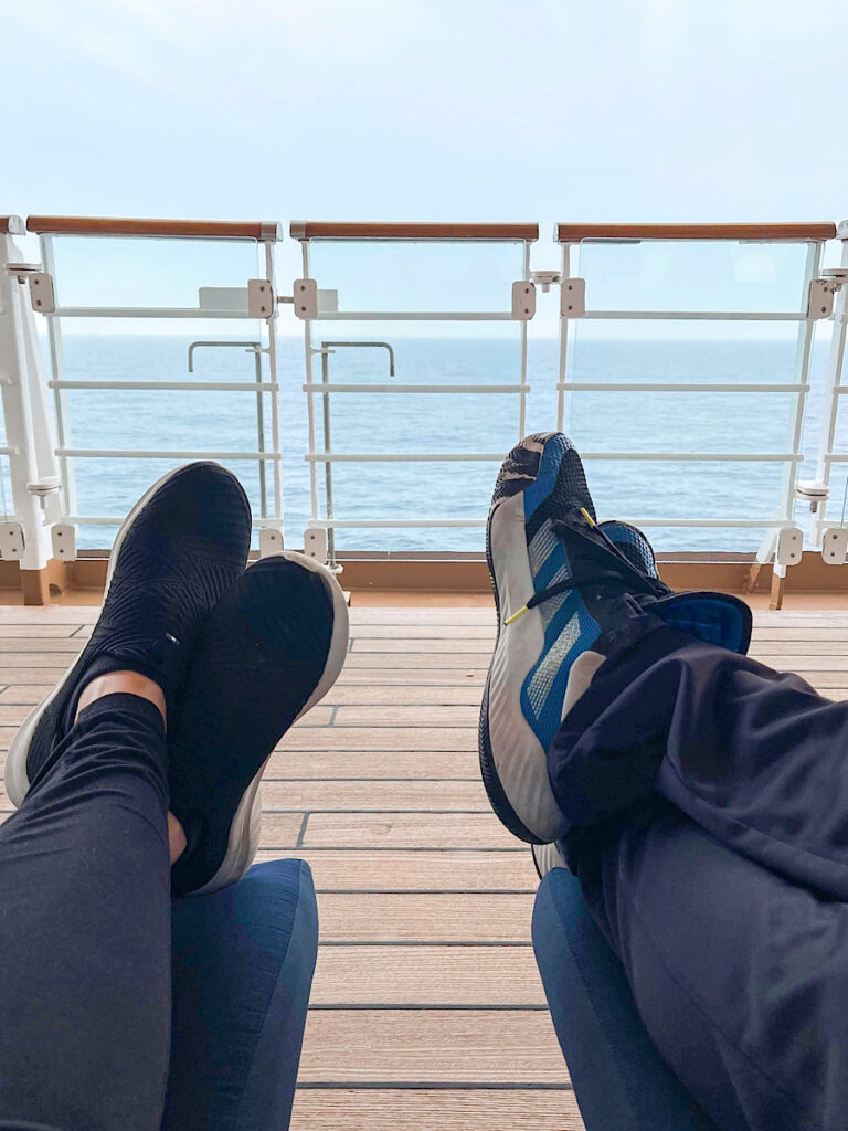 Two sets of legs in front of a glass wall on Deck 4 of the Disney Magic.