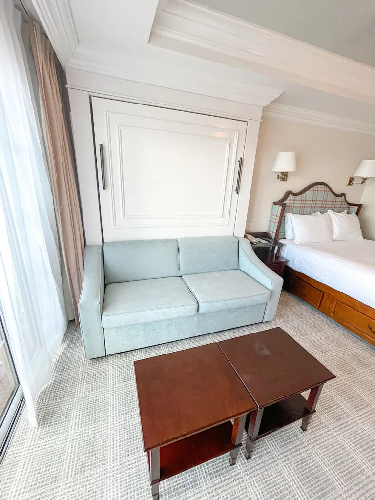 A small blue couch and coffee table next to a queen size bed at Disney's Grand Floridian.