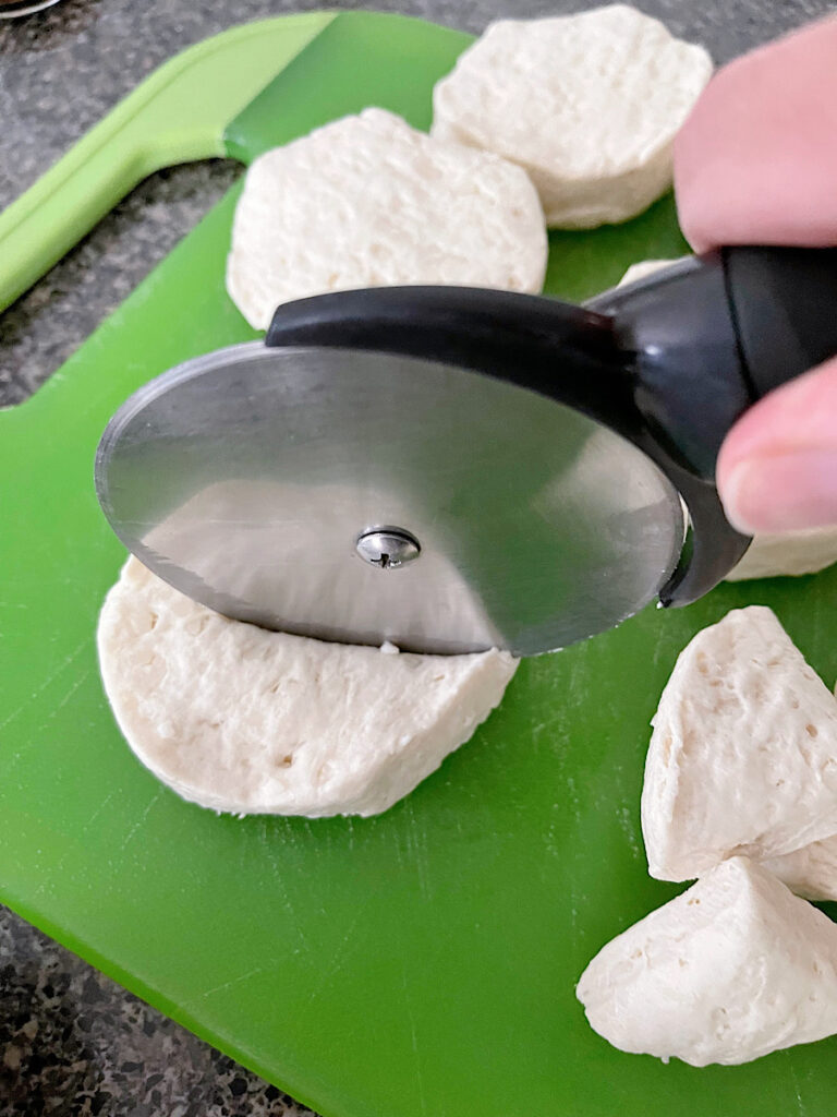 A pizza cutter cutting biscuit dough into pieces.