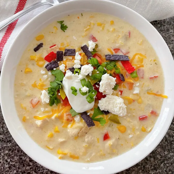 A bowl of Mexican Corn Chowder with sour cream, cilantro, green onion, and tortilla strips.