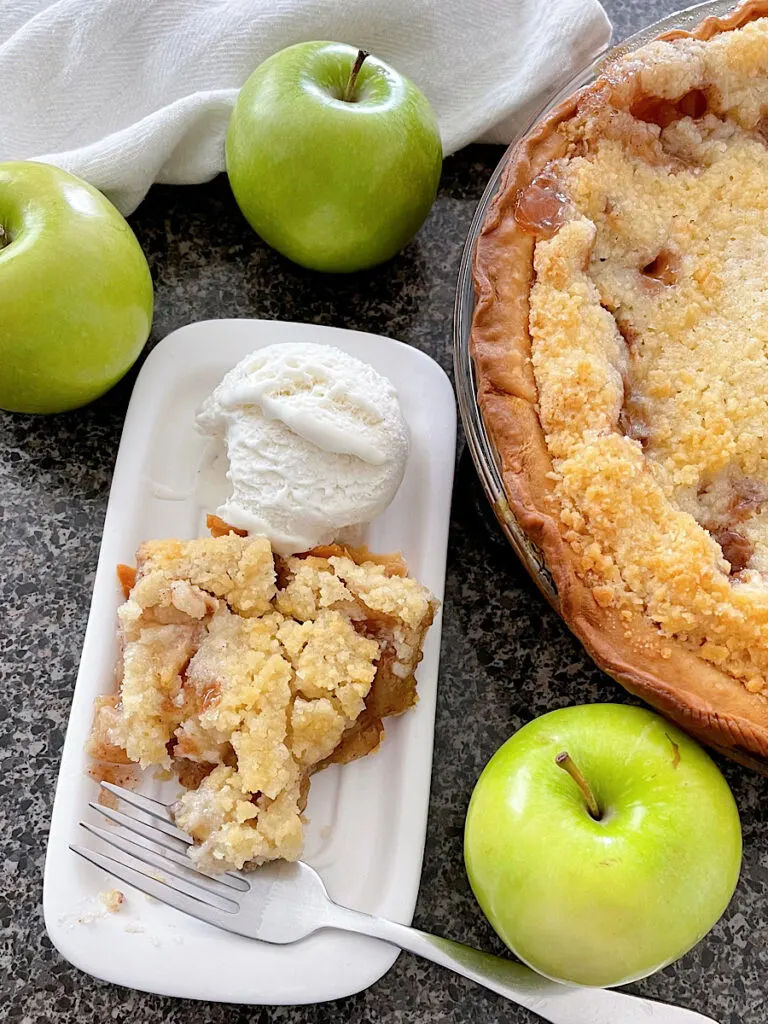 A slice of Dutch apple pie with three green apples and a scoop of ice cream.