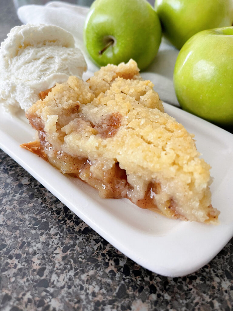 A slice of Dutch apple pie with three green apples and a scoop of ice cream.