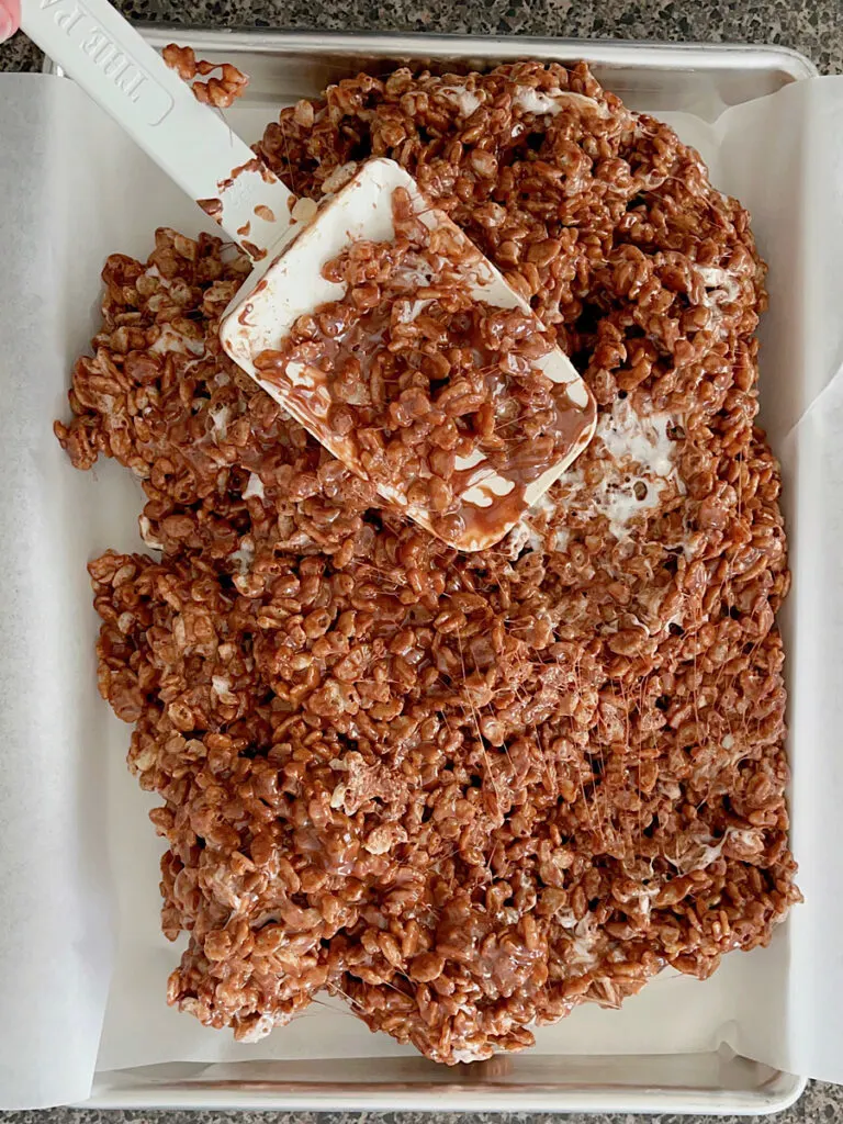 Chocolate rice krispy treats being spread in a pan.