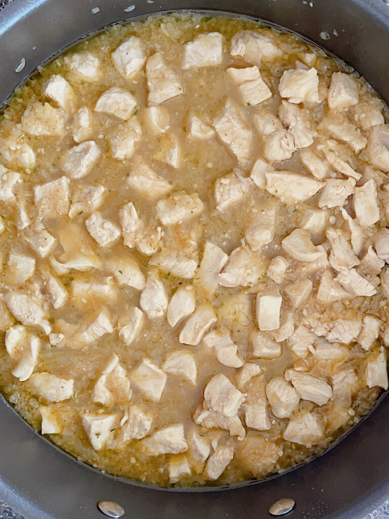 Chicken cooking in a soup pot with chicken stock and spices.