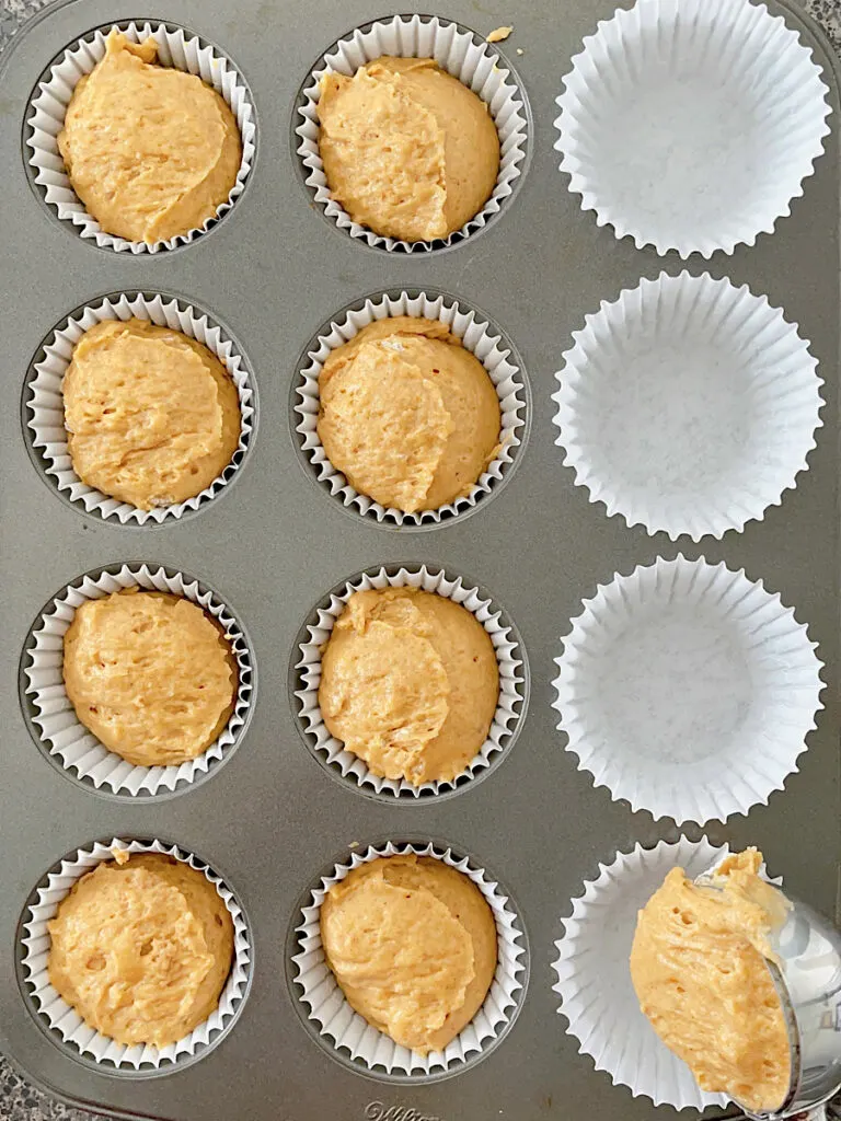 Pumpkin muffin batter scooped into baking liners in a muffin tin.
