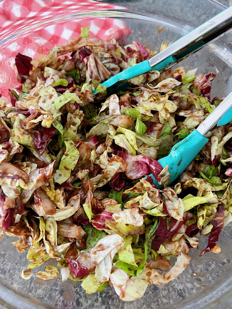 Chopped lettuce tossed with BBQ vinaigrette in a bowl with tongs.