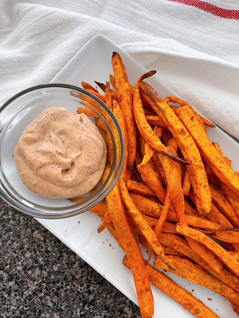 Sweet potato fries on a white plate with fry sauce.