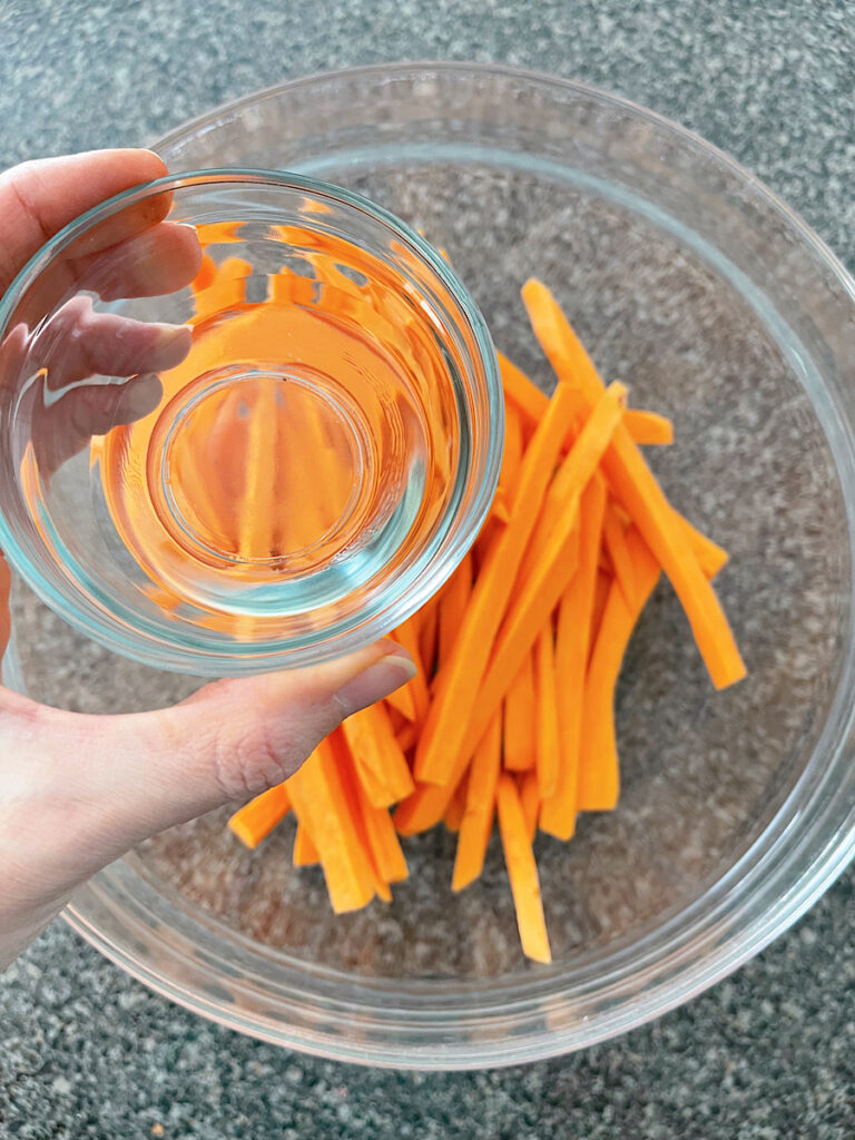 Sweet potato fries in a glass bowl with oil.