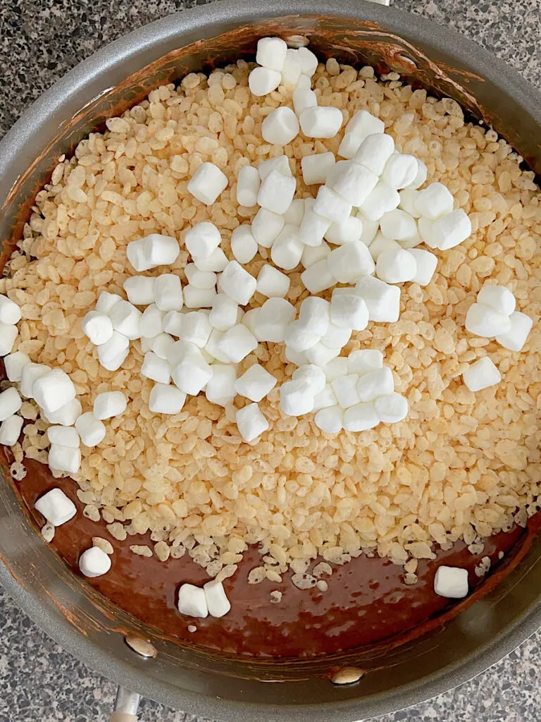 Melted marshmallows with chocolate, rice krispies, and whole marshmallows in a pan.