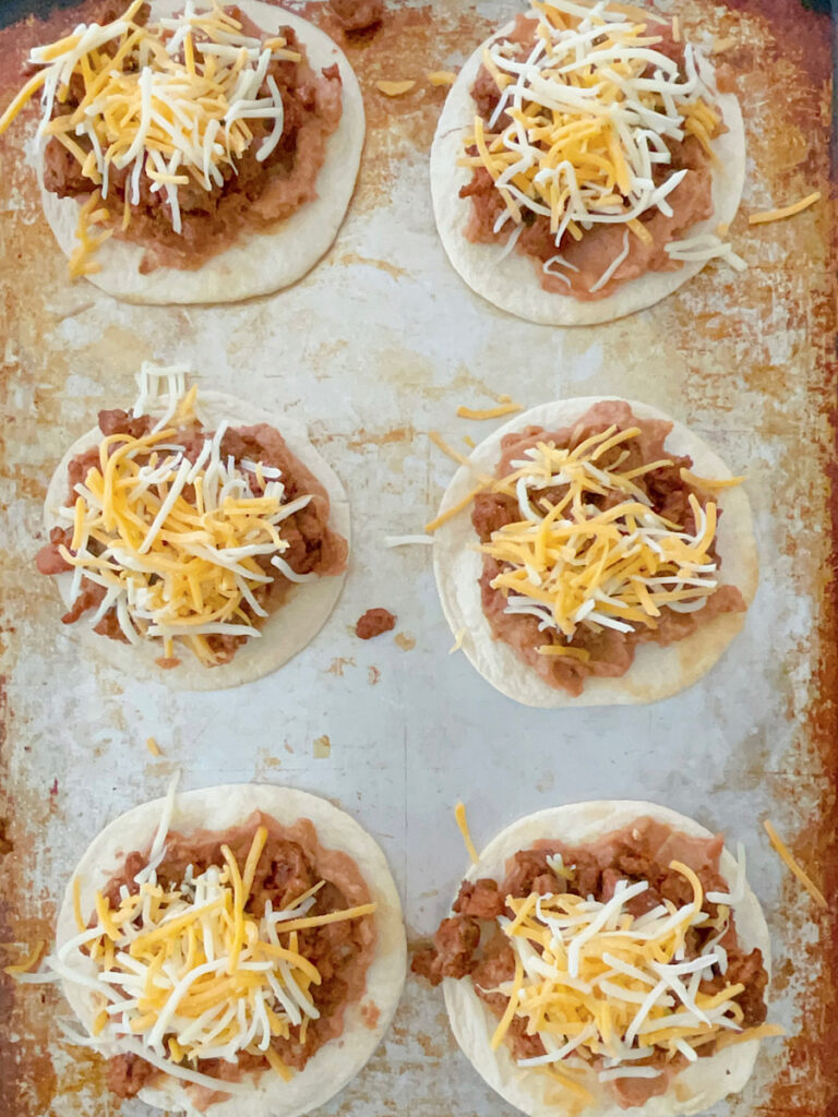 Tortillas with beans, meat, and cheese on a baking sheet.