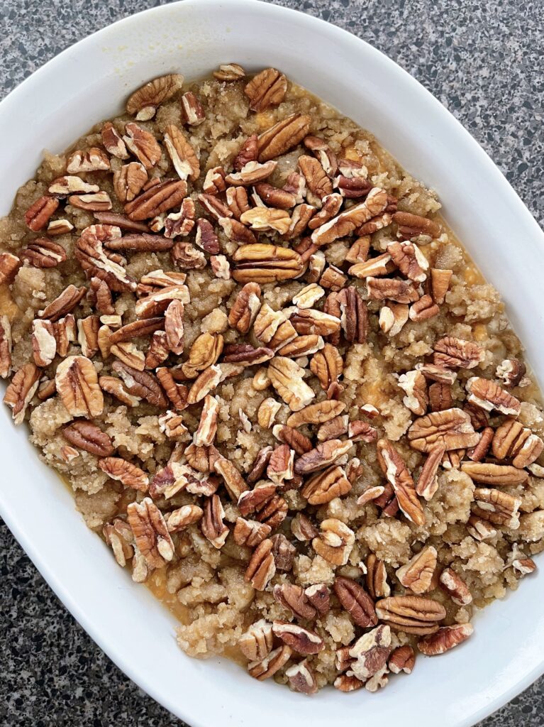 A dish of mashed yams topped with streusel and pecans.