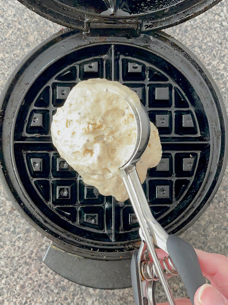 Waffle batter in a scoop over a greased waffle maker.