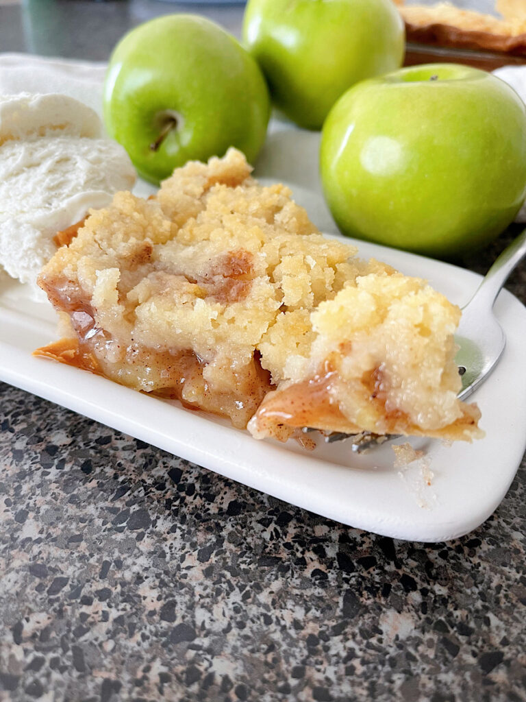 A slice of Dutch apple pie with three green apples and a scoop of ice cream.