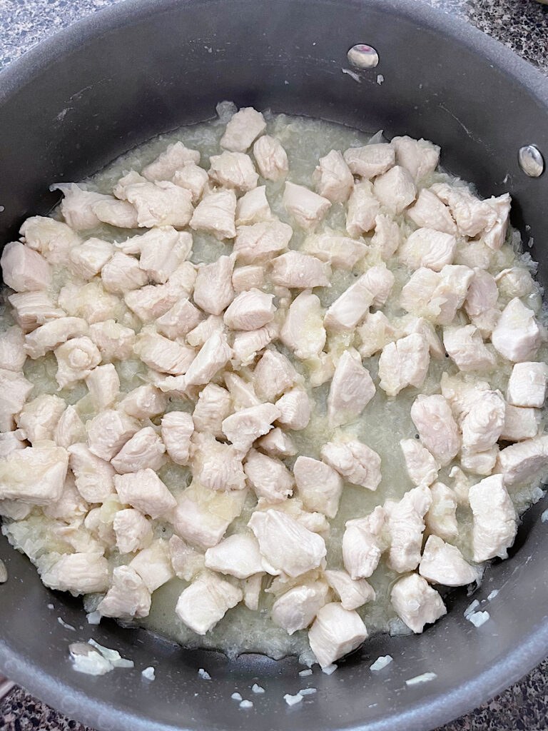 Pieces of chicken cooking in a pan with chopped onions and butter.