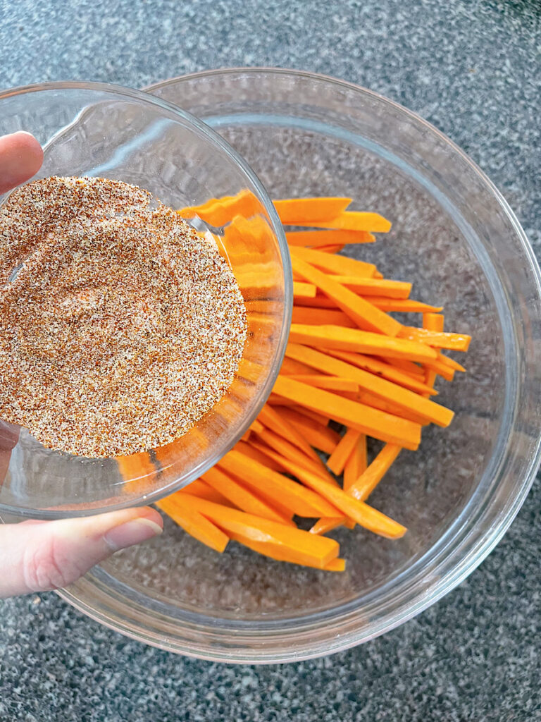 Sweet potato fries in a glass bowl with spices.