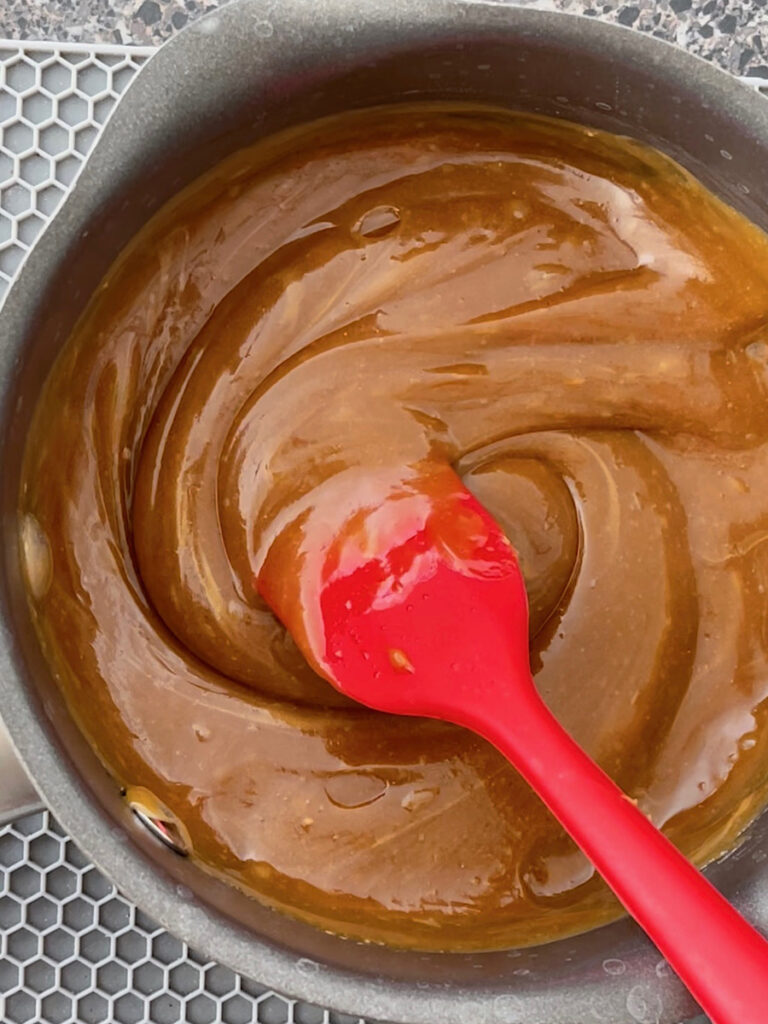 Peanut butter syrup in a saucepan with a red spatula.