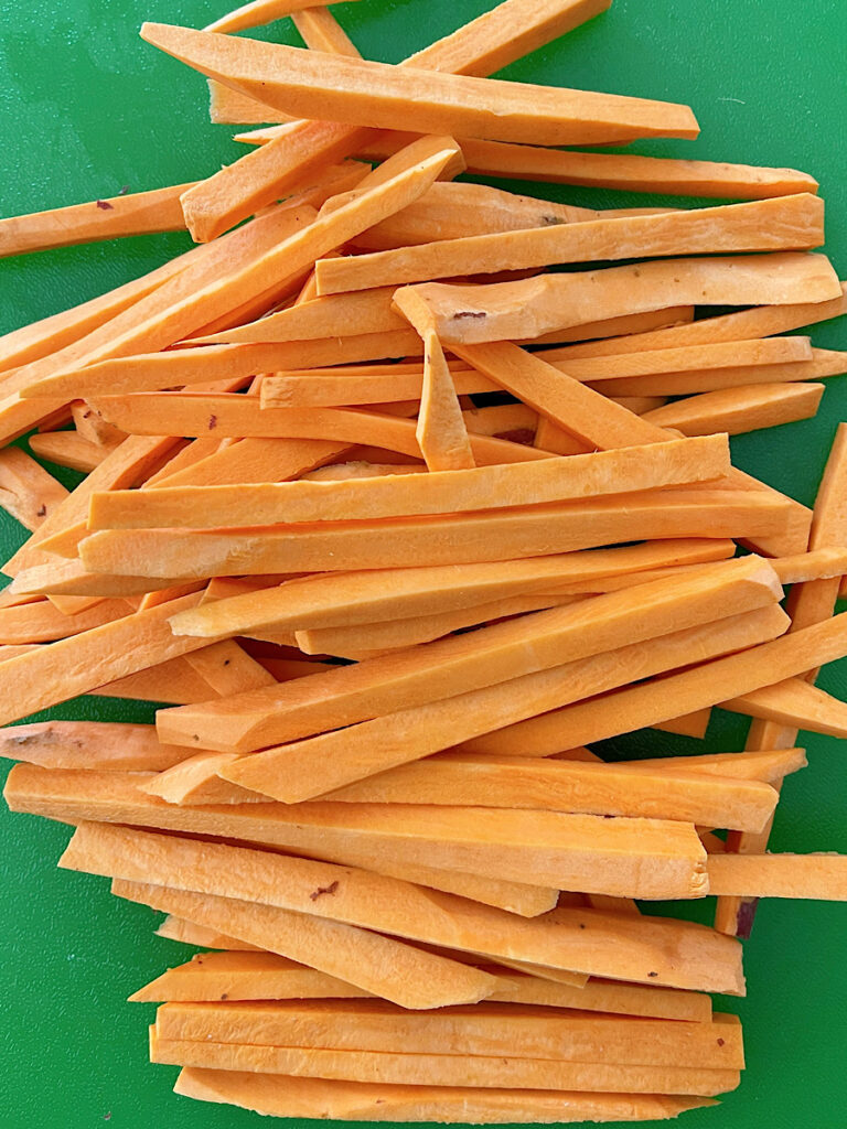 Sweet potatoes cut into fries on a cutting board.