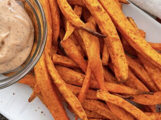 Sweet potato fries on a white plate with fry sauce.