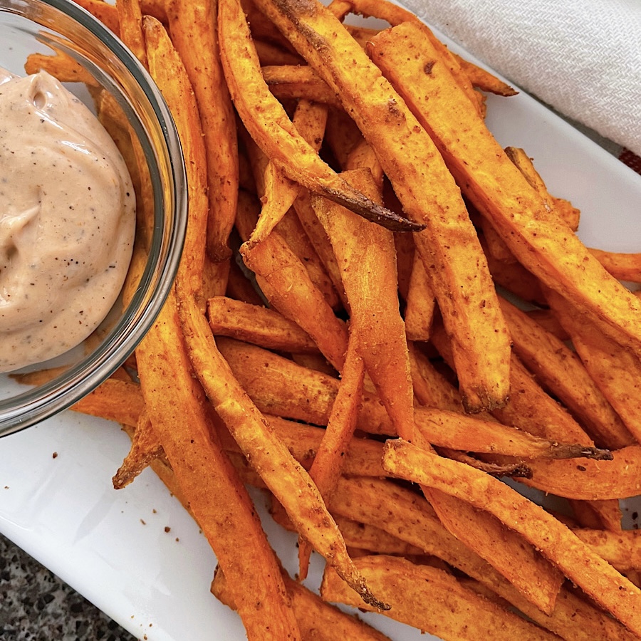 Sweet potato fries on a white plate with fry sauce.