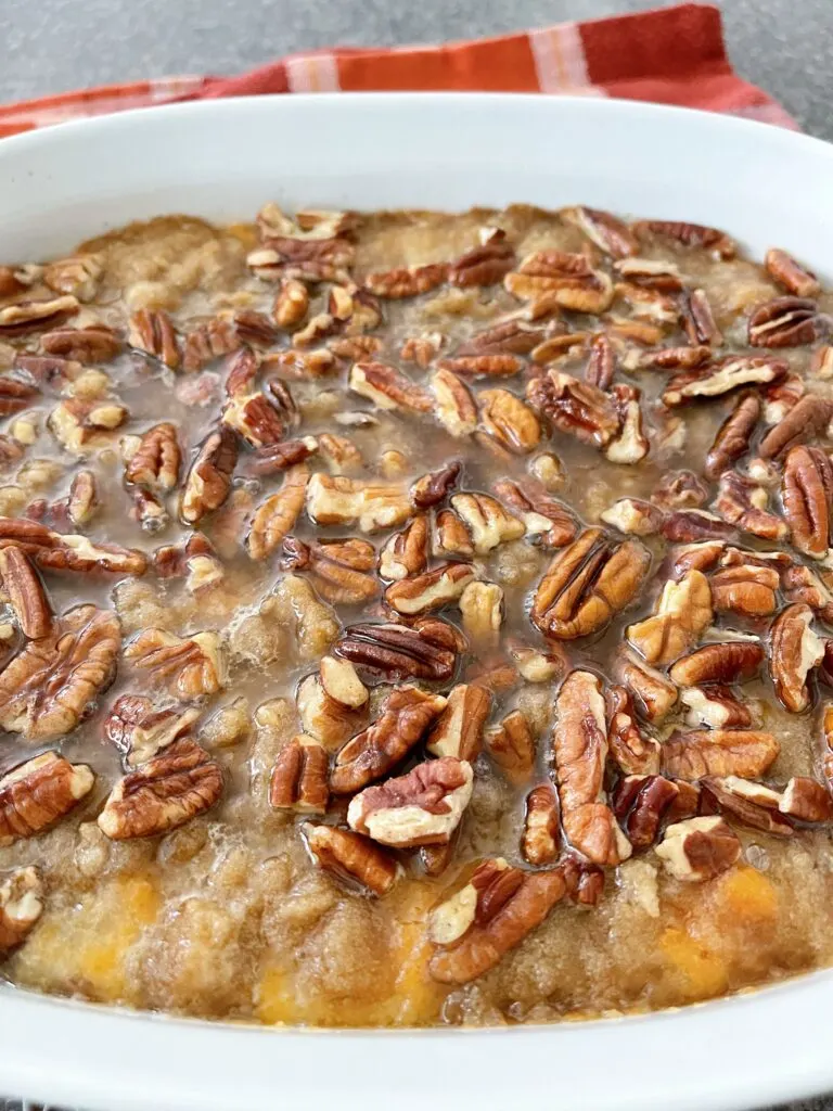 A dish of mashed yams topped with streusel and pecans.