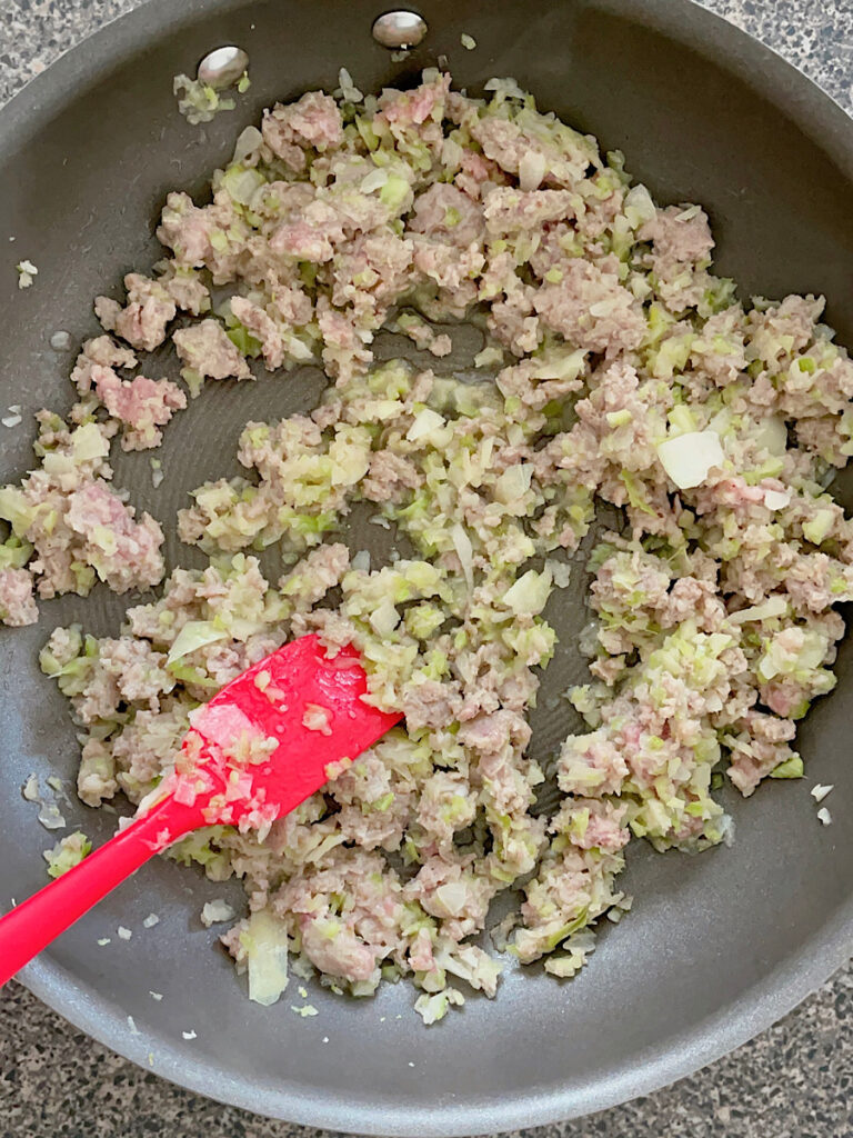 Chopped onions, celery, and ground pork in a pan.